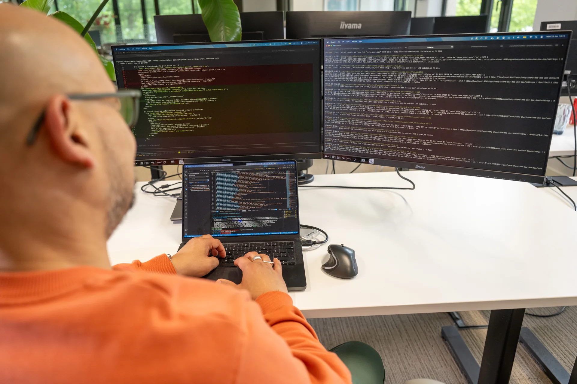 Ontwikkelaar met dubbele monitors en laptop met code-editor