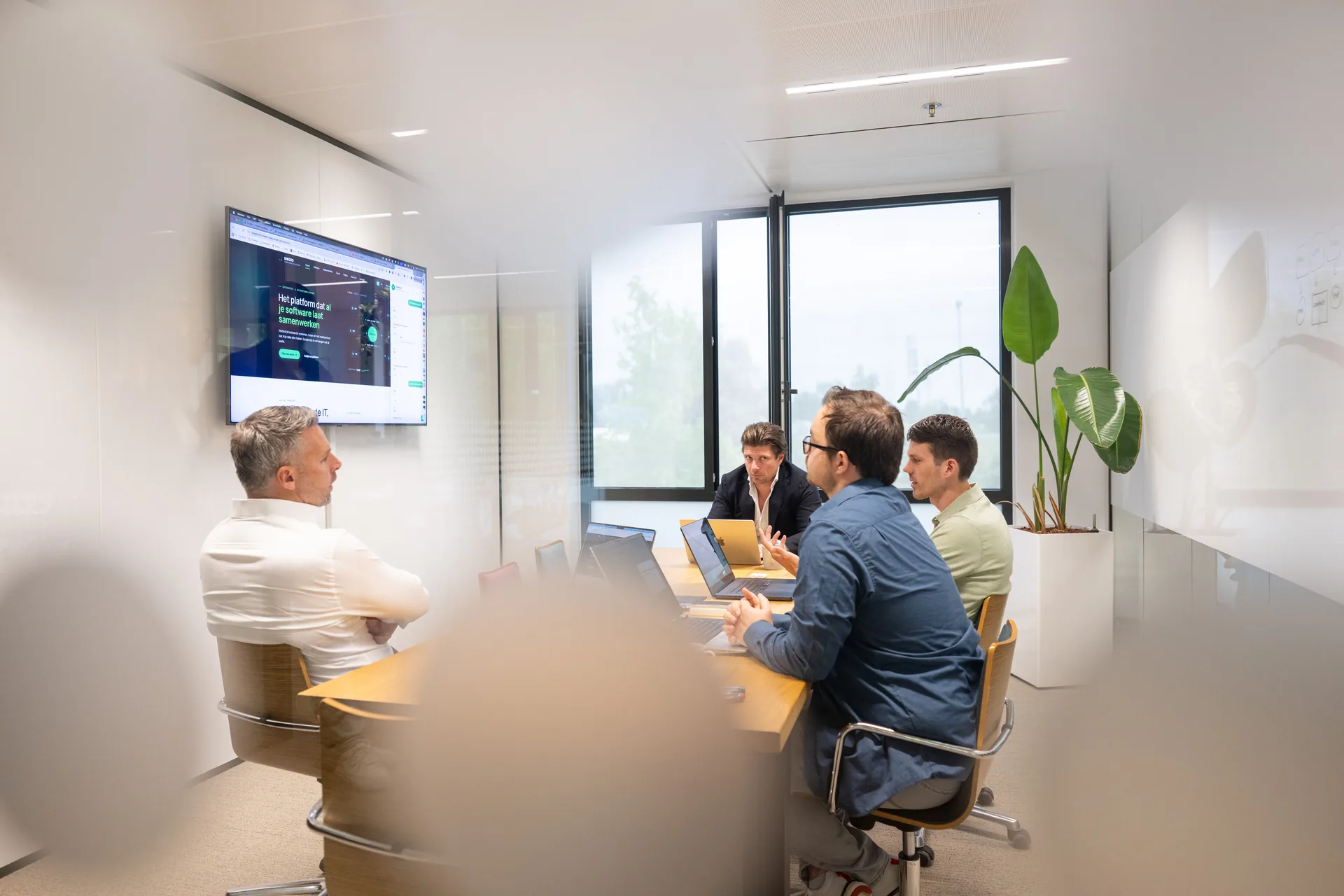 Emendis-team overlegt bij een tv-scherm met code, plant op de voorgrond